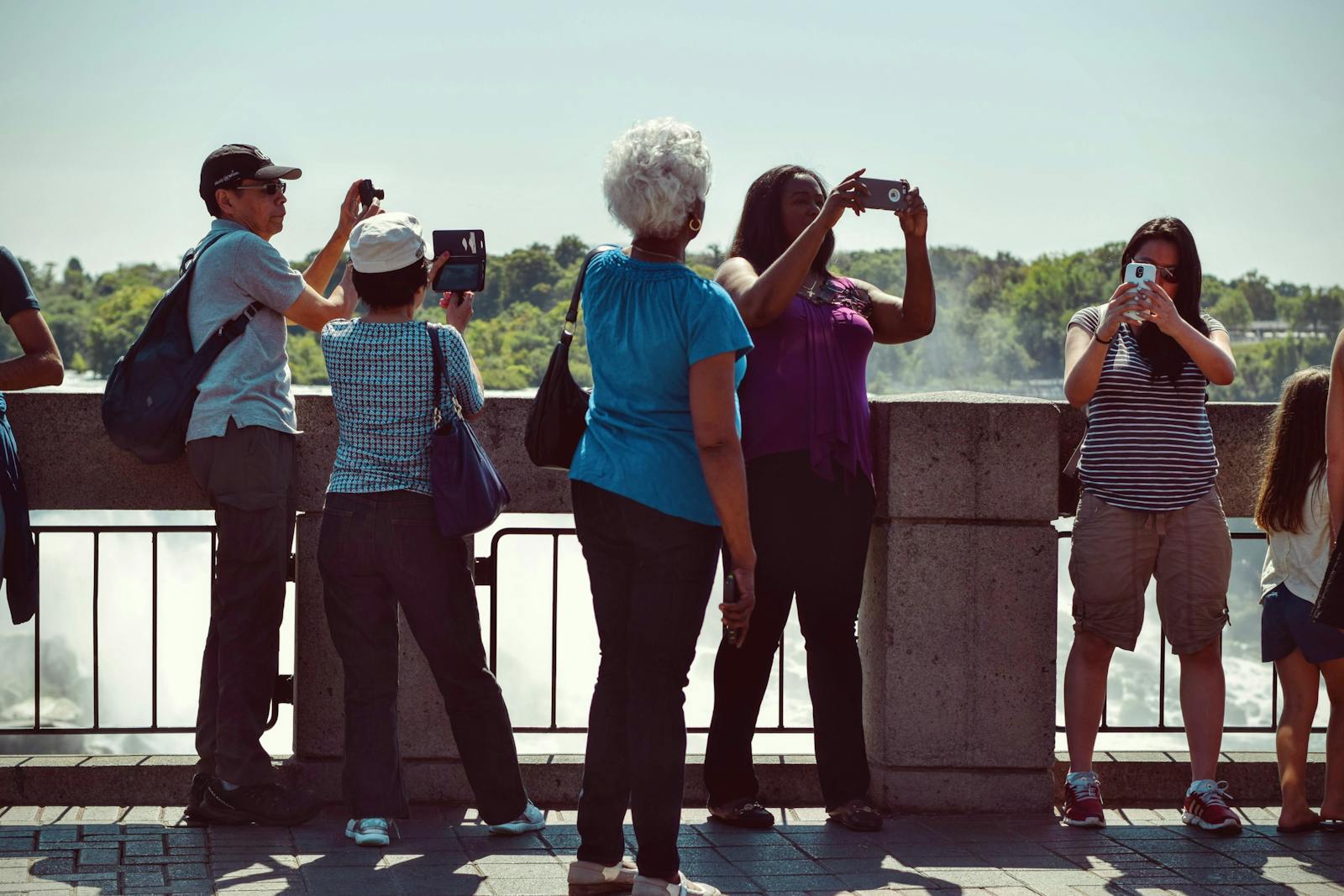 Group of diverse tourists using smartphones to capture scenic outdoor views on a sunny day.