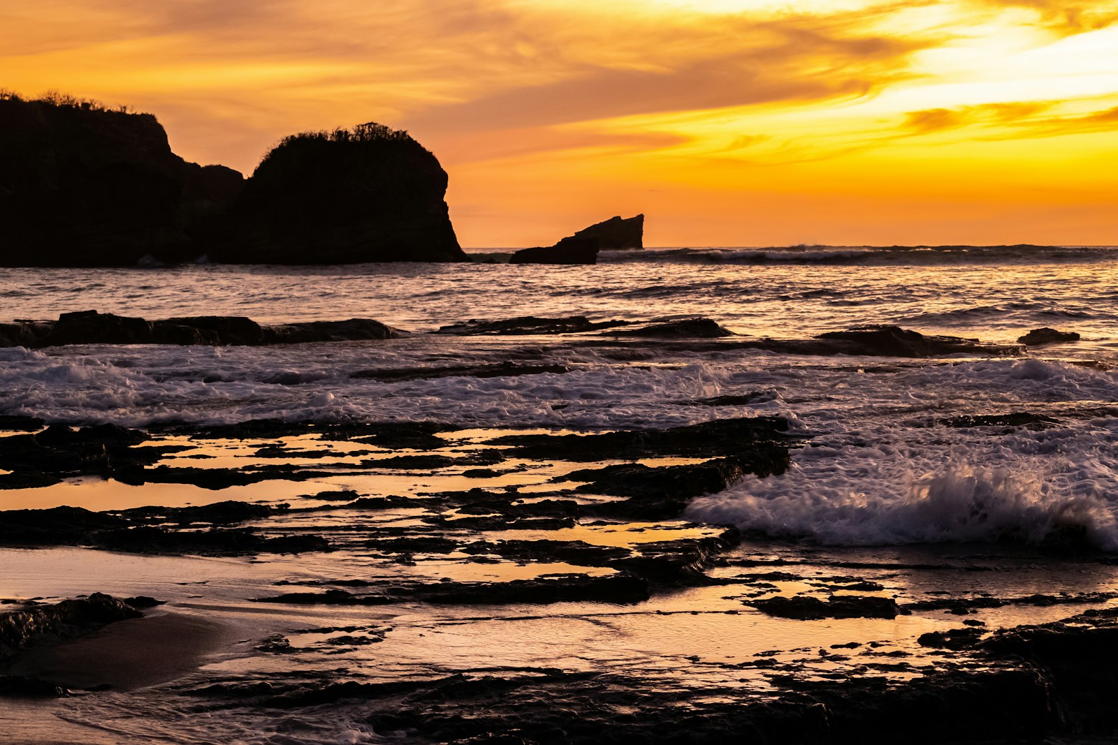 a sunset over the ocean with waves crashing on the rocks