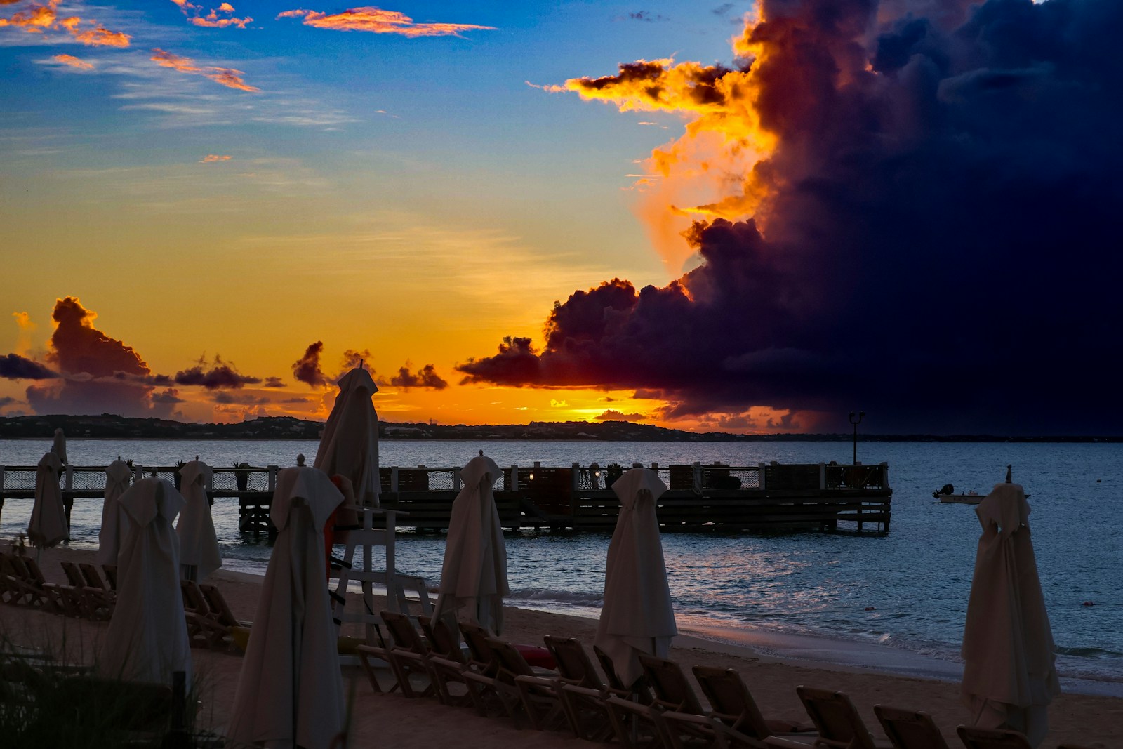 The sun is setting over the beach with umbrellas