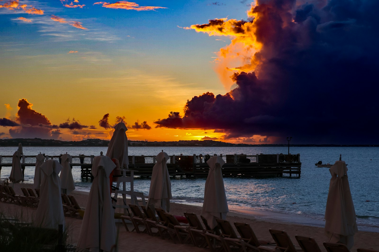 The sun is setting on the beach with chairs and umbrellas